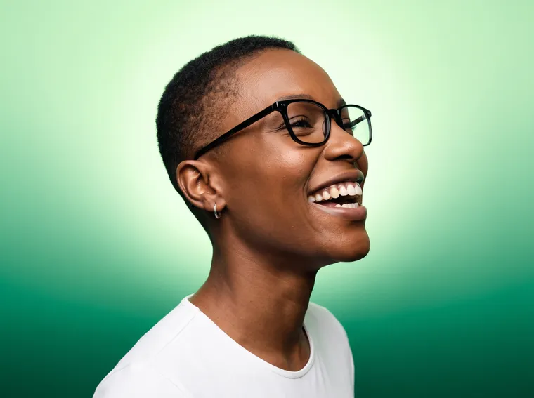 Mulher de óculos rindo de perfil, iluminada por um glow verde radial